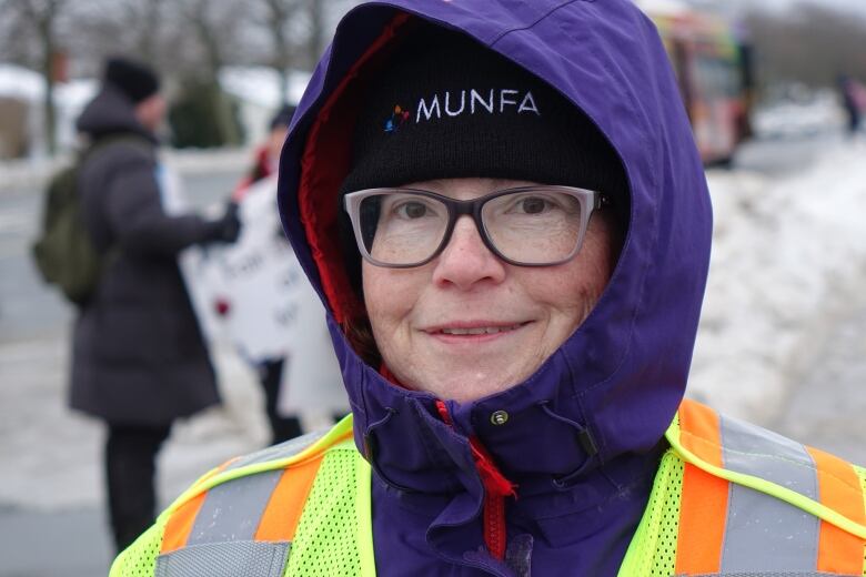 A close-up of a person wearing a safety vest and hat with a MUNFA logo. They're smiling.