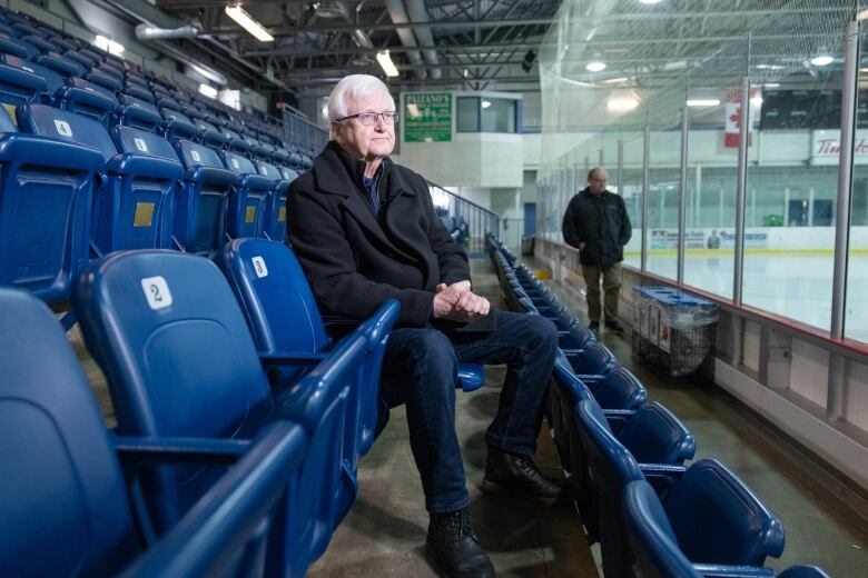 A man sits in a seat overlooking the ice rink at an arena.