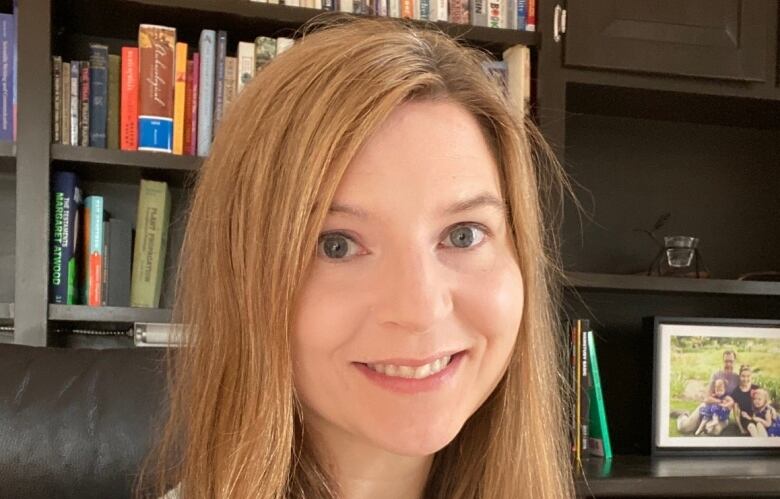 A woman sitting in an office with books in the background.