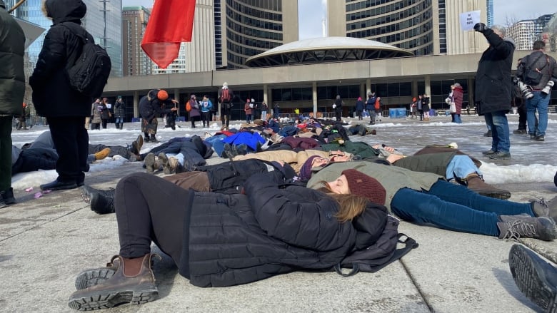 Advocates for the unhoused take part in a 'die-in' at Toronto City Hall on Monday, Feb. 6, 2023. They are urging city council to expand the hours of its warming centres until April to help prevent injuries and death to people experiencing homelessness.