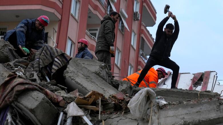 People atop a pile of rubble, one with a tool raised above his head as he tries to break away the rocks. 