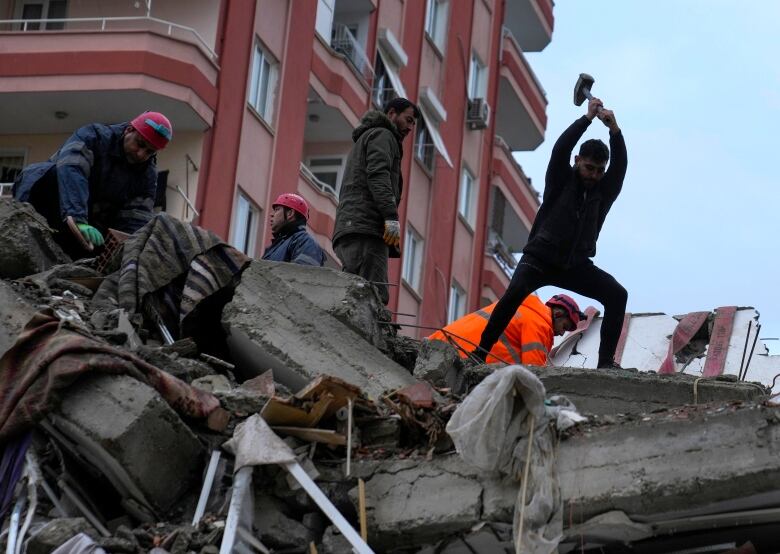 People atop a pile of rubble, one with a tool raised above his head as he tries to break away the rocks. 