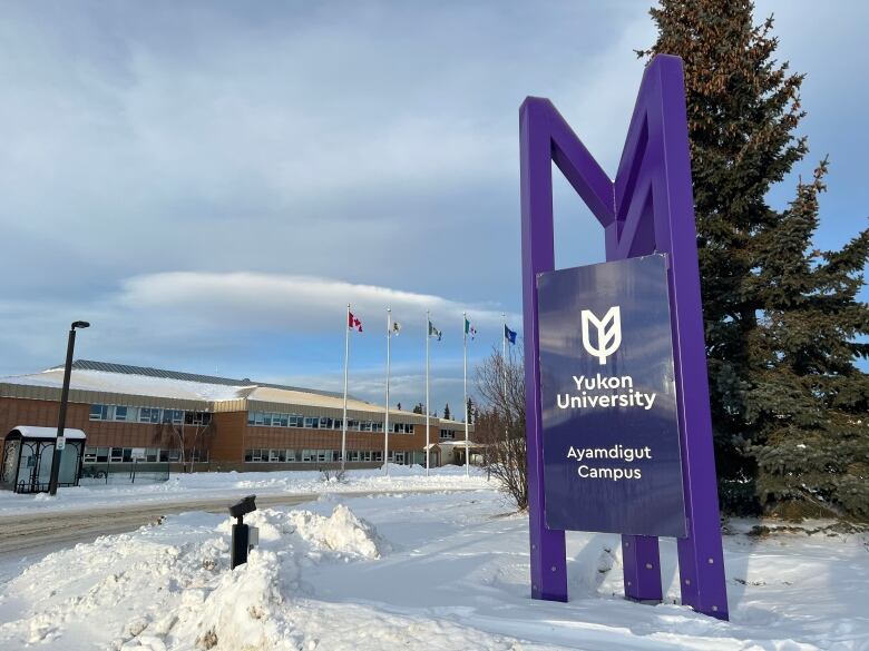 A sign reading, 'Yukon University Ayamdigut Campus' is seen in front of a building and a row of flags.