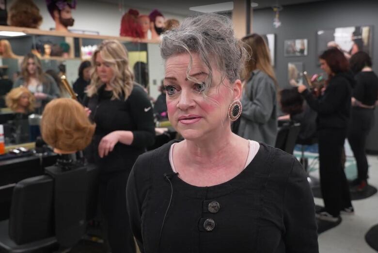 A woman stands with a bunch of women behind practising how to cut hair in a student salon.