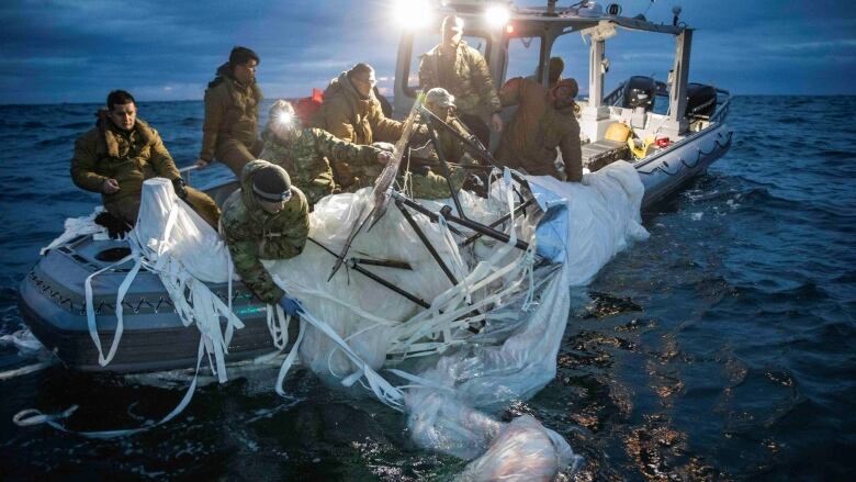 Close up shot of a small boat with about 8 people on board, pulling a large white item out of the water.