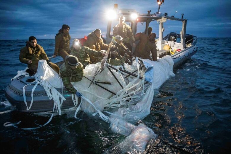 Close up shot of a small boat with about 8 people on board, pulling a large white item out of the water.