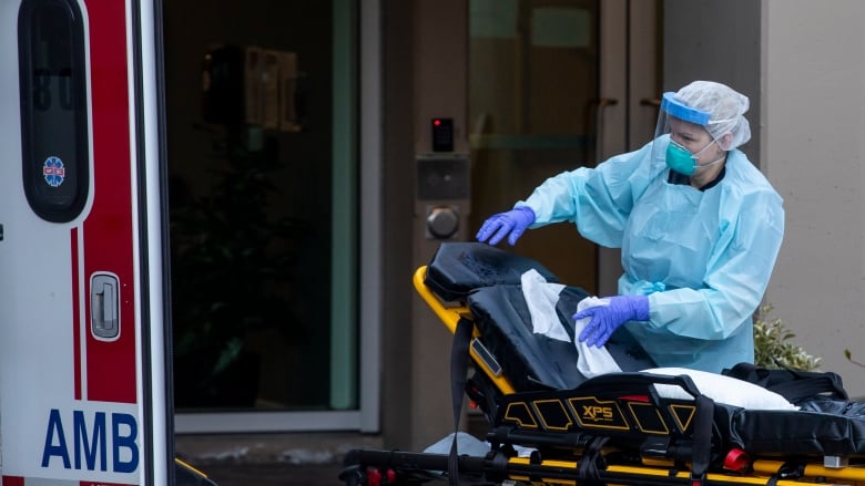 Paramedics wearing full body protective equipment clean a stretcher