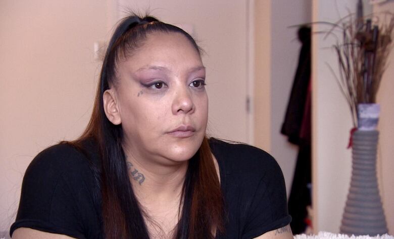 A woman with a black shirt sits in a room for an interview with a plant in the background.