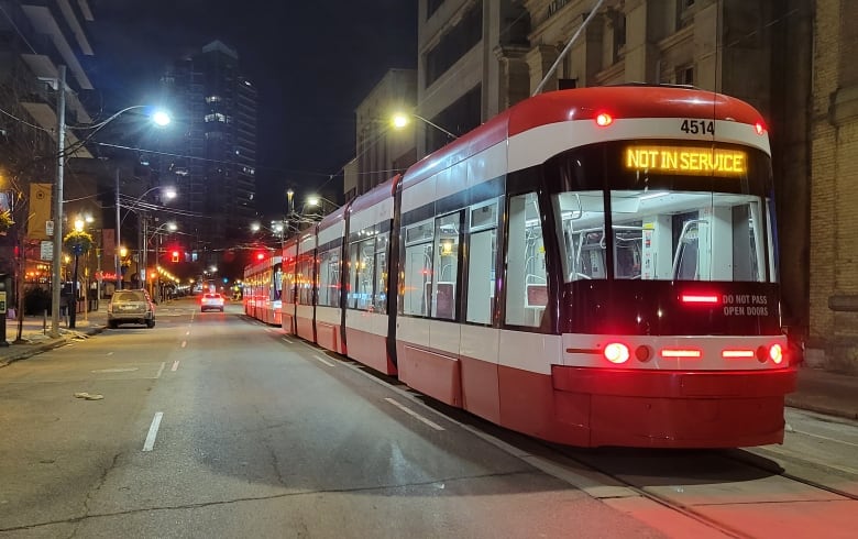 A streetcar with a 'not in service sign' is stopped in the street at night.