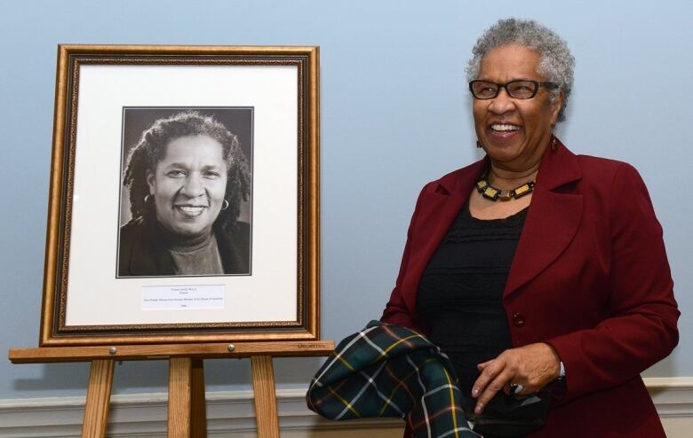 A smiling woman with glasses stands beside a picture of herself.