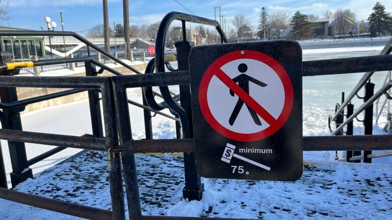 A sign on a locked gate to a frozen waterway.