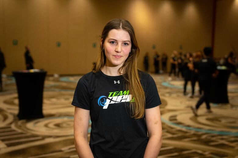 A girl stands in a hotel ballroom in a Team P.E.I. shirt. 