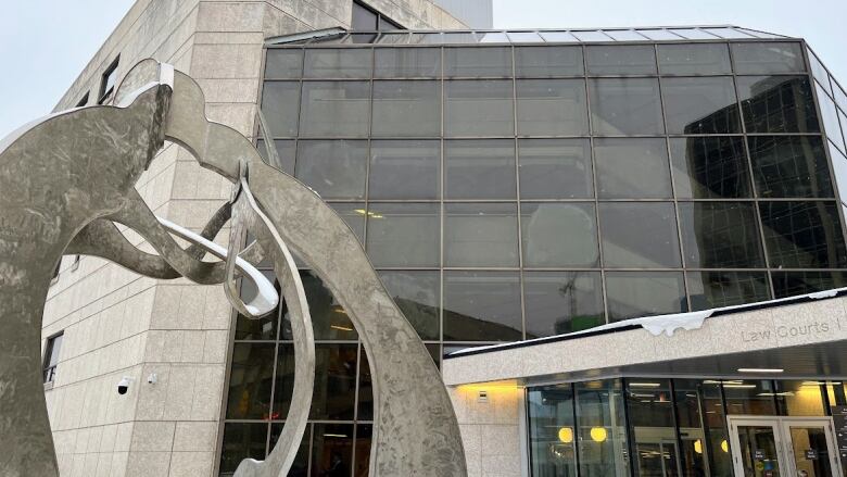 A building with several right angles, lots of glass and Tyndall stone. An abstract silver metal sculpture stands in front.