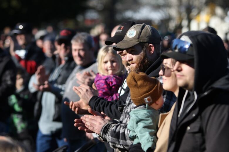 A man holding a baby stands in a line at a rally.