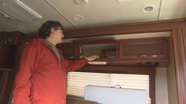 A person in an RV reaches up to grab something from a cabinet.