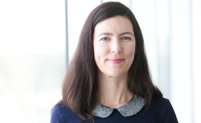 A middle-aged white woman with dark brown hair smiles in a professional photoshoot. 