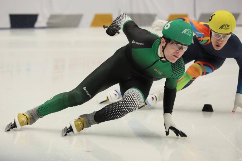 Two speed skaters go around a curve on an indoor ice surface. 