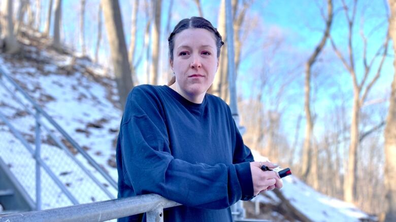 A woman in workout clothes stands at a railing on a set of outdoor stairs. There's snow on the ground and trees behind her.