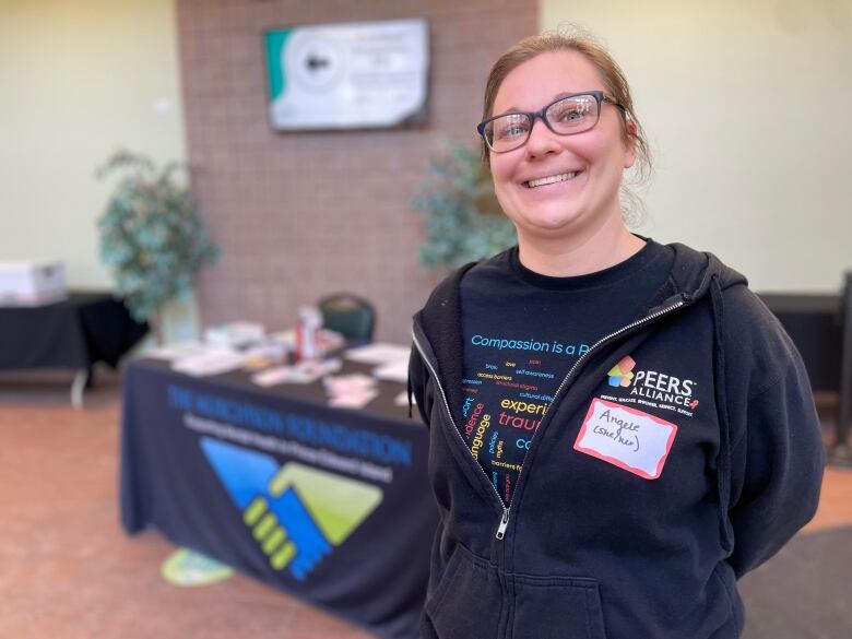 A smiling woman stands in front of a table holding pamphlets.