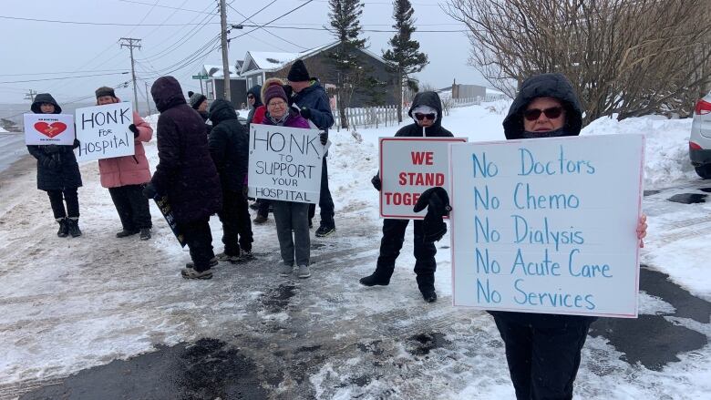 Several people stand outside holding signs. The closest sign says 