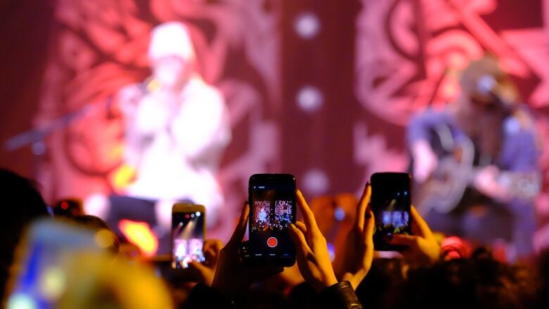 A person uses an iPhone to film a musician on a stage.