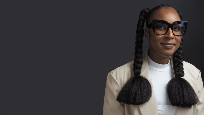 A Black woman with two thick braids and very large eyeglasses smiles at the camera.