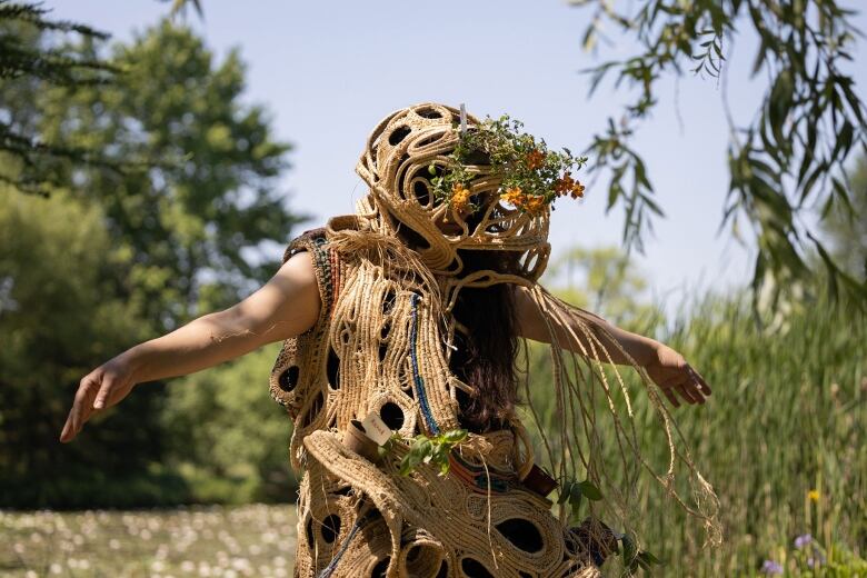 A performance artist wearing a dress constructed from handmade paper and plants.