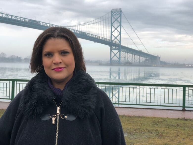 A woman wearing a black jacket standing in front of a suspension bridge