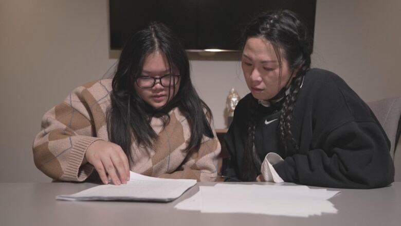 Two women sit at a table, reading documents. 