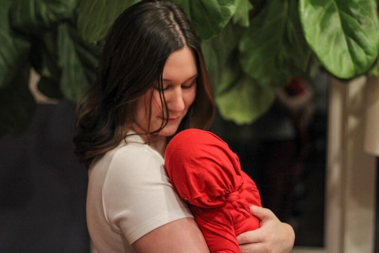 A woman wearing a white t-shirt holds a baby wearing a red outfit.