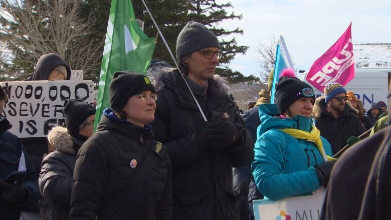 A group of people wearing winter clothing hold flags and signs. 