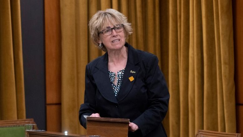 A woman in black stands at a podium.