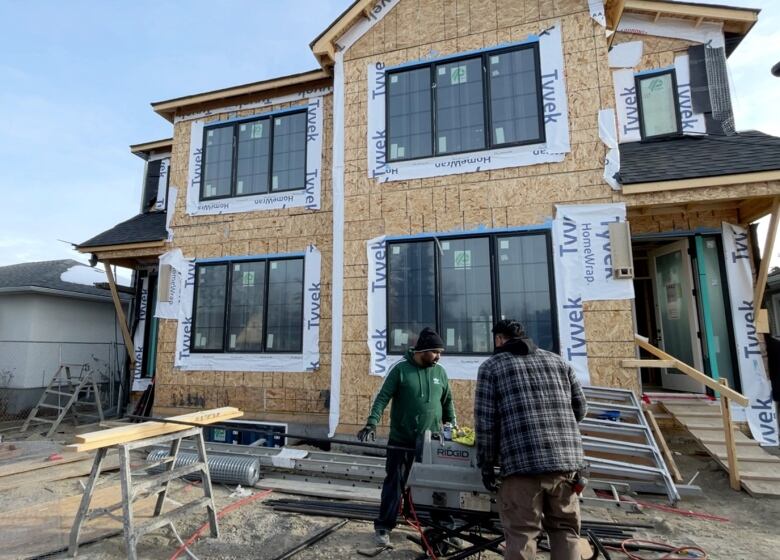 Two workers stand in front of a two-storey duplex under construction in the southwest community of Shaganappi.