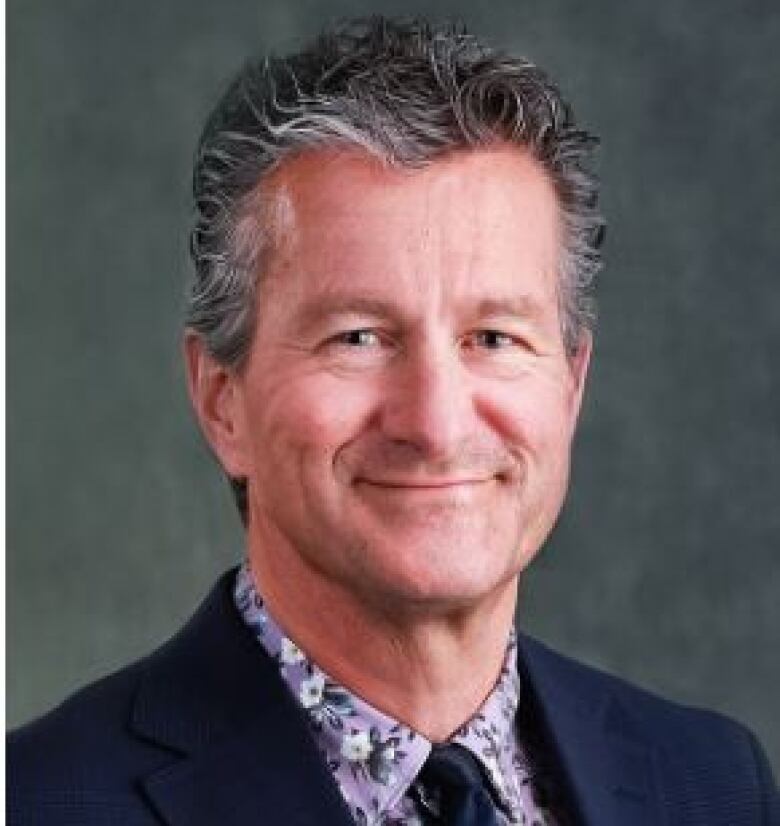 A man in business attire smiles at the camera.