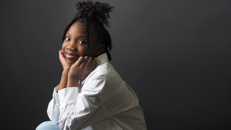 A young Black girl rests her chin on her hands, smiling at the camera.