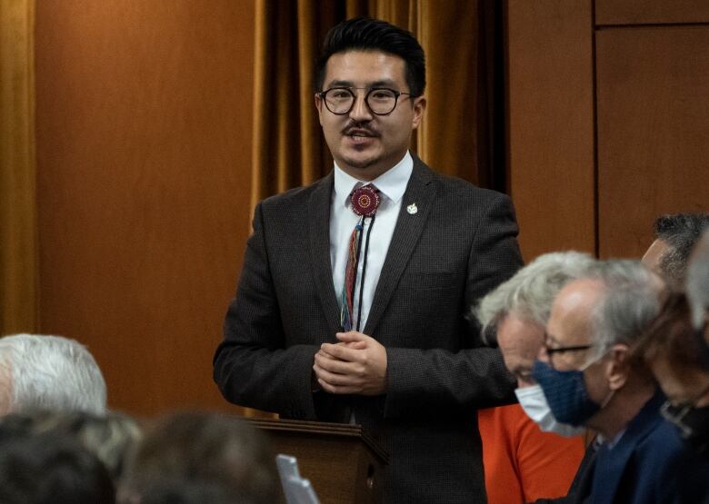 A man in a suit speaks in a crowd.