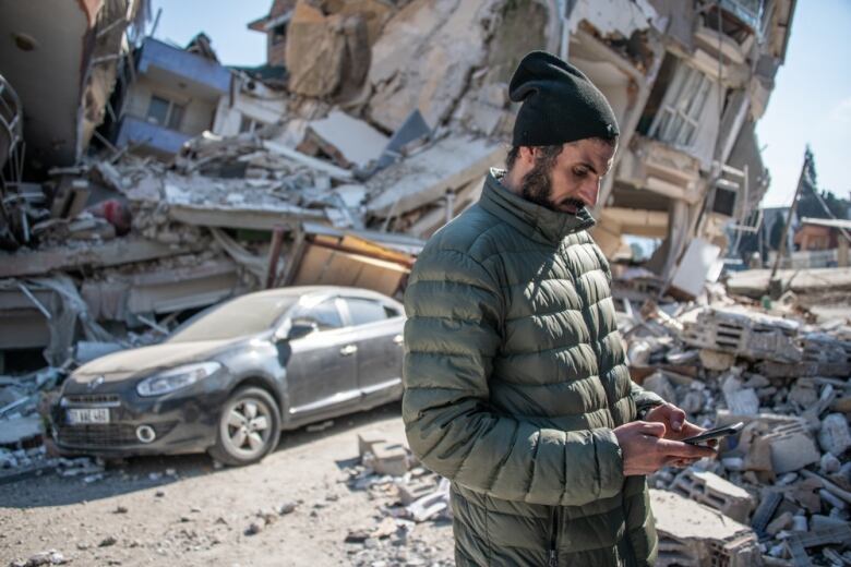 A man looks at his phone in a street destroyed by an earthquake in Turkey.