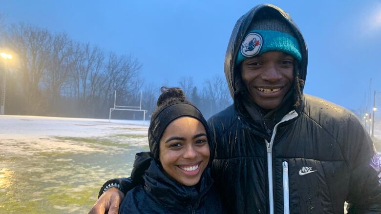 Olivia Ghosh-Swaby and her partner Bleska Kambamba coach the Western women's football team. They're standing at the field at Western University on a cold and rainy day. 