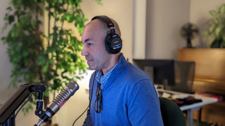 A bald man wearing headphones speaks into a microphone.