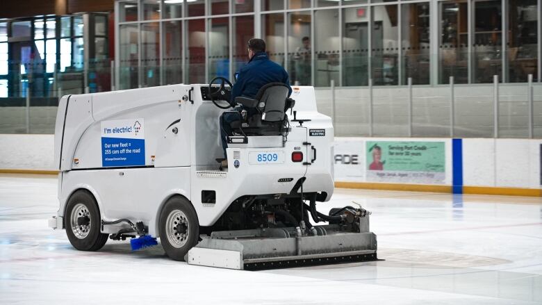 An electric ice resurfacer is seen from behind smoothing the ice at an indoor arena.