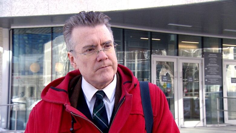 A man in a red jacket stands in front of the entrance to the provincial courthouse.