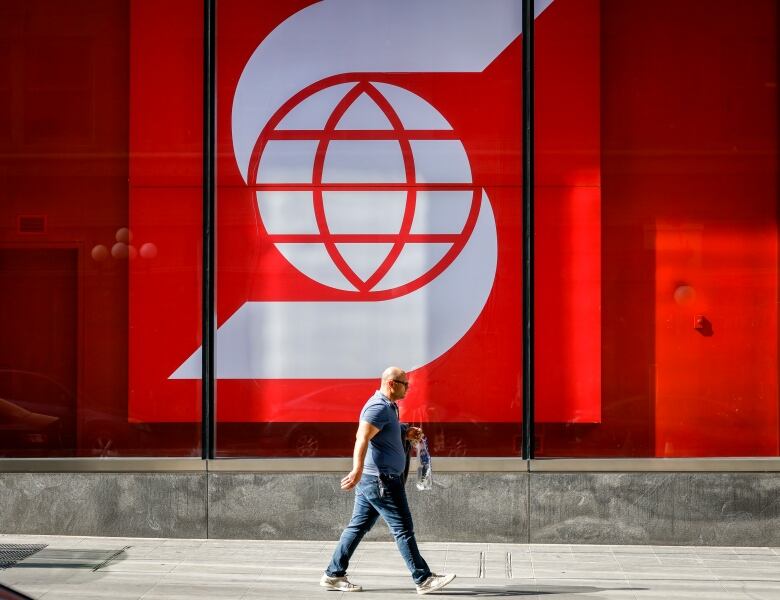 A man walks by a large photo of the Scotiabank logo.