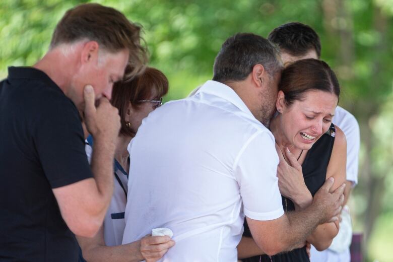 A woman cries as she is held by a group of people around her. People hold tissues in their hands. 