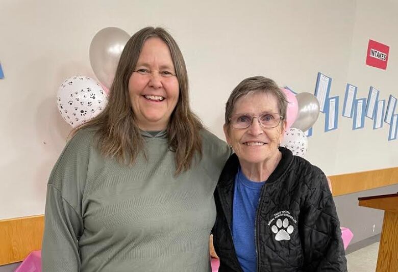 Two women wrap their arms around each other's shoulders and smile.