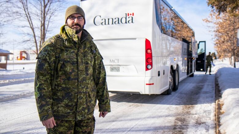 A soldier stands in front of a bus that says Canada.