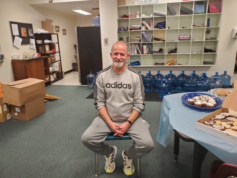 A man in an Adidas shirt sits on a chair in front of the camera