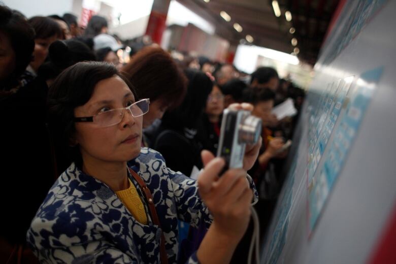 A middle-aged Chinese woman looks at posters posted on a wall listing eligible bachelors at a matchmaking event in China.