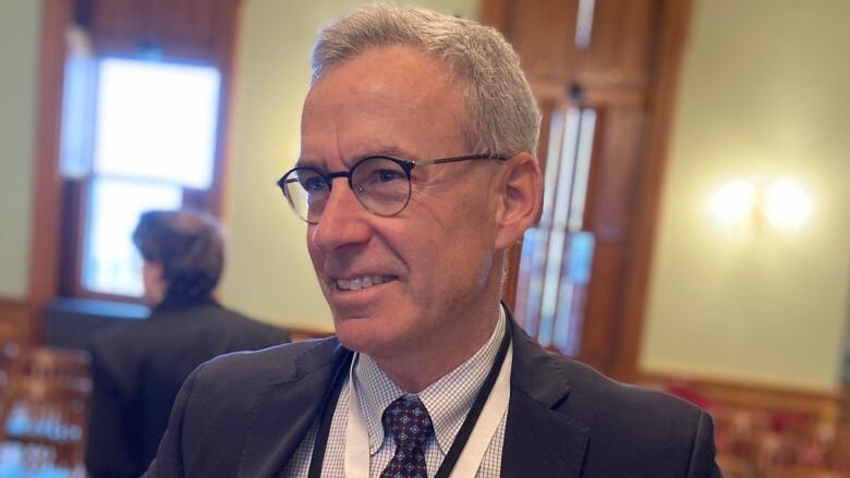 Head and shoulders picture of a grey-haired man wearing glasses and an indentification lanyard. 