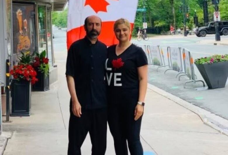 A man and woman stand in fronf of the Canadian flag under a board that reads Turkish Delight. 