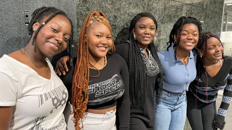 Four girls and one woman stand against a wall, smiling for the camera